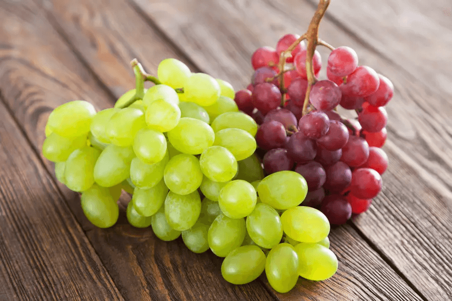 Deux grappes de raisins blanc et noir fraichement posés sur une table en bois